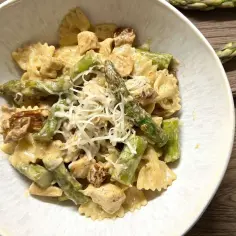 Pyszna pierś z kurczaka ze szparagami w sosie śmietanowym, podana z makaronem farfalle i posypana parmezanem.