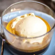 Pyszne affogato: gałka lodów waniliowych w gorącym espresso, podana w szklance na niebieskim talerzyku.