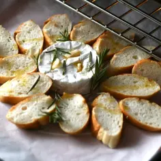 Pieczony camembert z czosnkiem i rozmarynem, otoczony kromkami bagietki, gotowy do zapieczenia.