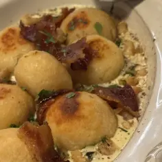 Pyszne pierogi ruskie, przepis babci, polane śmietaną i posypane skwarkami.