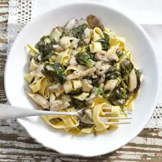 Tagliatelle z kremowym sosem z boczniaków i szpinakiem, posypane pieprzem. Pyszne danie gotowe do podania.