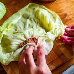 Ręce zwijają gołąbki z farszem mięsnym w liście kapusty. Idealny przepis na gołąbki na 1kg mięsa.