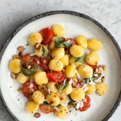 Pyszne makaron gnocchi z pomidorkami koktajlowymi, szałwią i orzechami na talerzu.