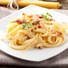 Spaghetti carbonara - przepis oryginalny ze śmietaną. Pyszne danie z makaronem, boczkiem i pietruszką na białym talerzu.
