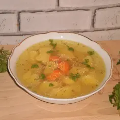 Aromaticzny rosół z ziemniakami i marchewką, ozdobiony natką pietruszki, podany w białej miseczce na drewnianej desce.
