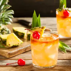 Orzeźwiający drink Mai Tai z ananasem i wiśnią, podany na drewnianym stole.