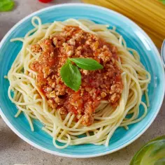 Spaghetti z sosem bolognese na niebieskim talerzu, ozdobione bazylią.