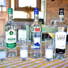 Trzy butelki i kieliszki z greckim trunkiem ouzo, gotowe do degustacji.