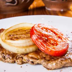 Karkówka pieczona w plastrach, z grillowaną cebulą i pomidorem. Pyszne danie, które można podać z majonezem i ketchupem.