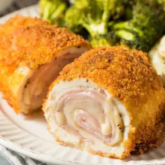 Złocisty kotlet po szwajcarsku z rozpływającym się serem i szynką, podany z puree ziemniaczanym i brokułami.