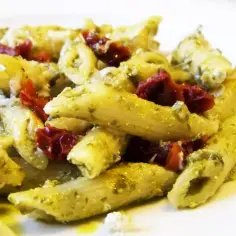 Penne makaron z pesto i suszonymi pomidorami, posypane parmezanem. Pyszne danie gotowe do spożycia.
