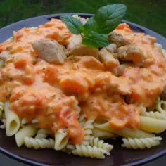 Penne i fusilli z kurczakiem w kremowym sosie pomidorowym z mascarpone, udekorowane listkiem bazylii.