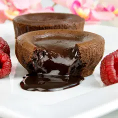 Płynna czekolada wypływa z gorącego ciasta brownie, ozdobionego malinami i kawałkami gorzkiej czekolady.