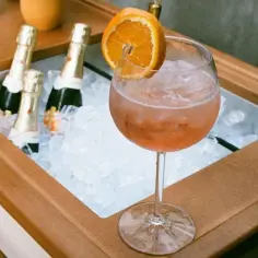 Idealne prosecco do Aperola? W chłodzącej lodowej kuwecie czekają butelki, a obok orzeźwiający drink z pomarańczą.