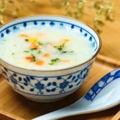 Miseczka z congee, ryżową owsianką z warzywami, obok łyżka na drewnianej tacce.