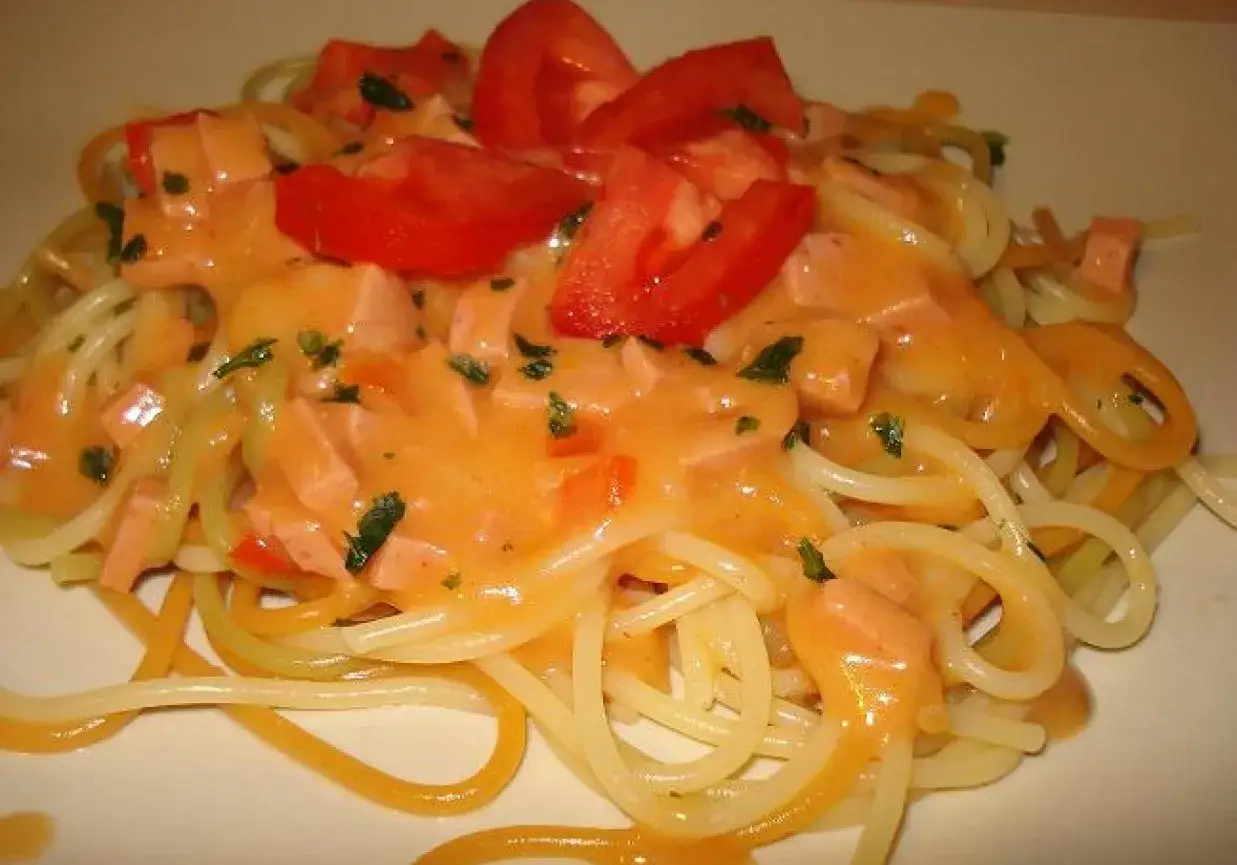 Pyszny makaron z sosem na bazie mascarpone, kawałkami wędliny i pomidorów, posypany natką pietruszki.