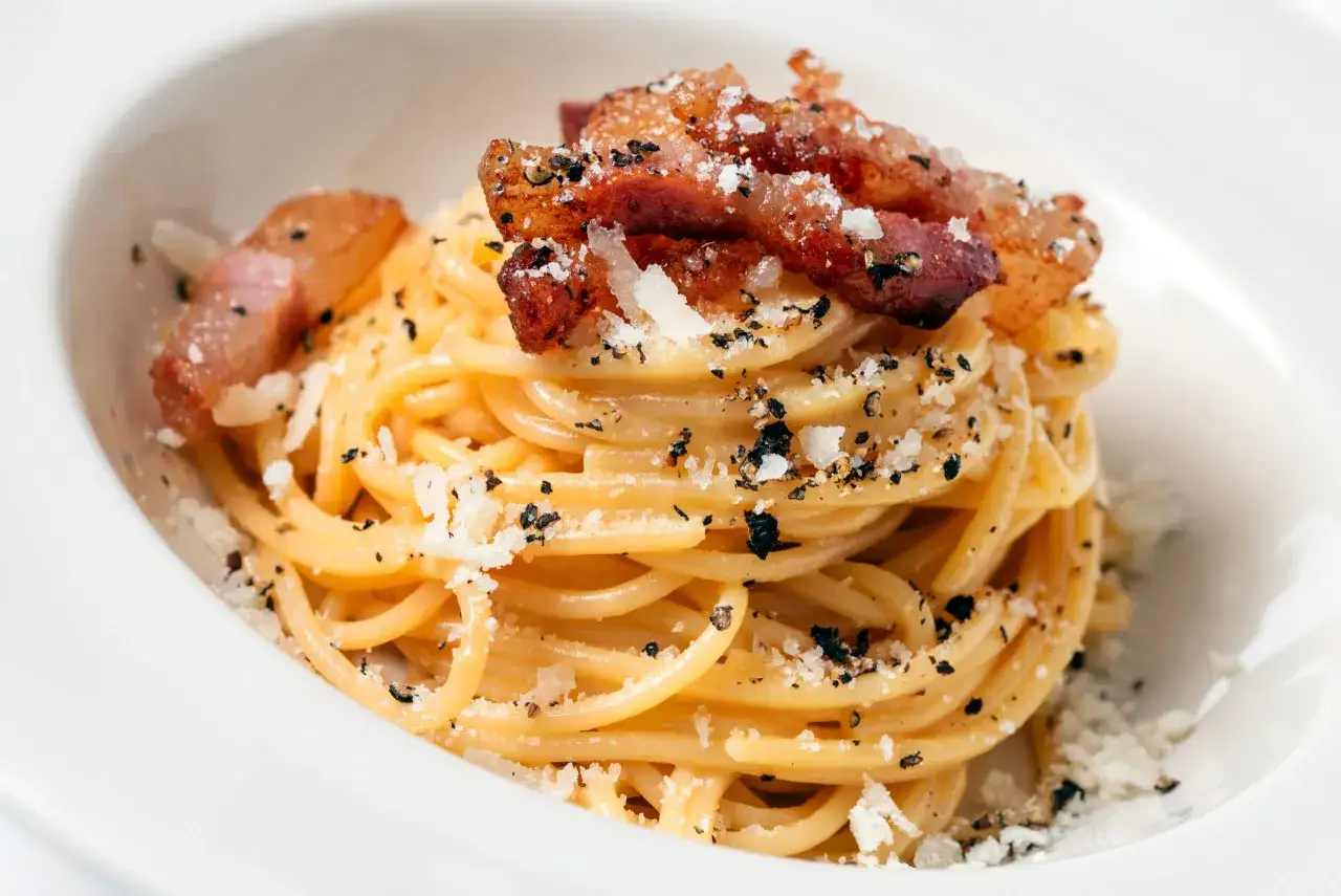 Spaghetti carbonara z chrupiącym guanciale, posypane parmezanem i pieprzem. To właśnie guanciale co to jest, sekretny składnik tej potrawy.