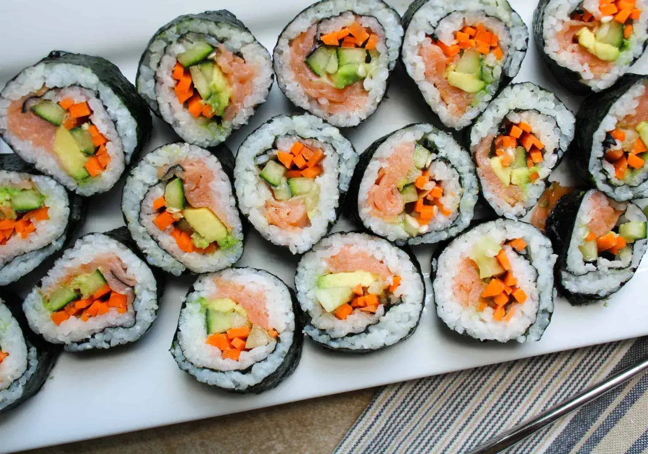 Ułożone na talerzu rolki sushi z łososiem, awokado, ogórkiem i marchewką. W środku widać kolorowe składniki, idealne do sushi.
