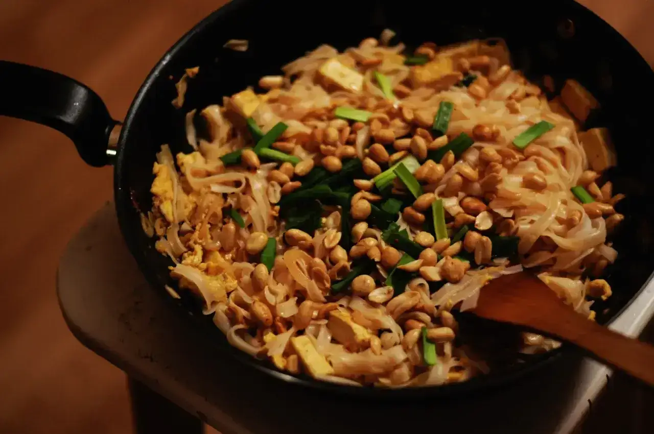 Gorący sos pad thai z makaronem ryżowym, tofu, orzeszkami ziemnymi i szczypiorkiem na patelni.