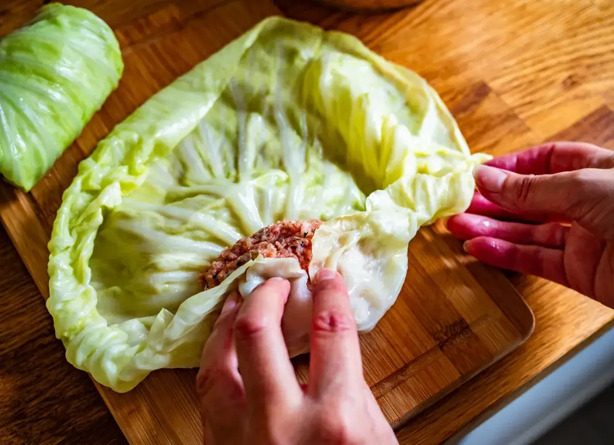 Ręce zwijają gołąbki z farszem mięsnym w liście kapusty. Idealny przepis na gołąbki na 1kg mięsa.