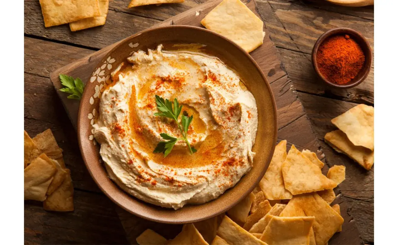 Pyszny hummus z ciecierzycy, polany oliwą i posypany papryką, podany z chrupiącymi kawałkami pity.
