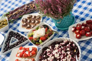 Pyszne greckie dania: sałatka grecka, oliwki, bruschetta z pomidorami, pieczone buraki z fetą i inne przekąski na niebiesko-białym obrusie.