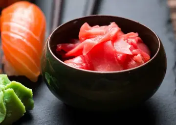 Różowy imbir do sushi w miseczce, obok kawałka łososia i zielonego wasabi. Idealny dodatek do japońskich przysmaków.