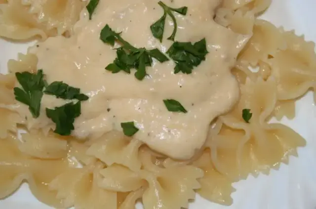 Pyszny makaron z parmezanem i kremowym sosem, udekorowany świeżą natką pietruszki.